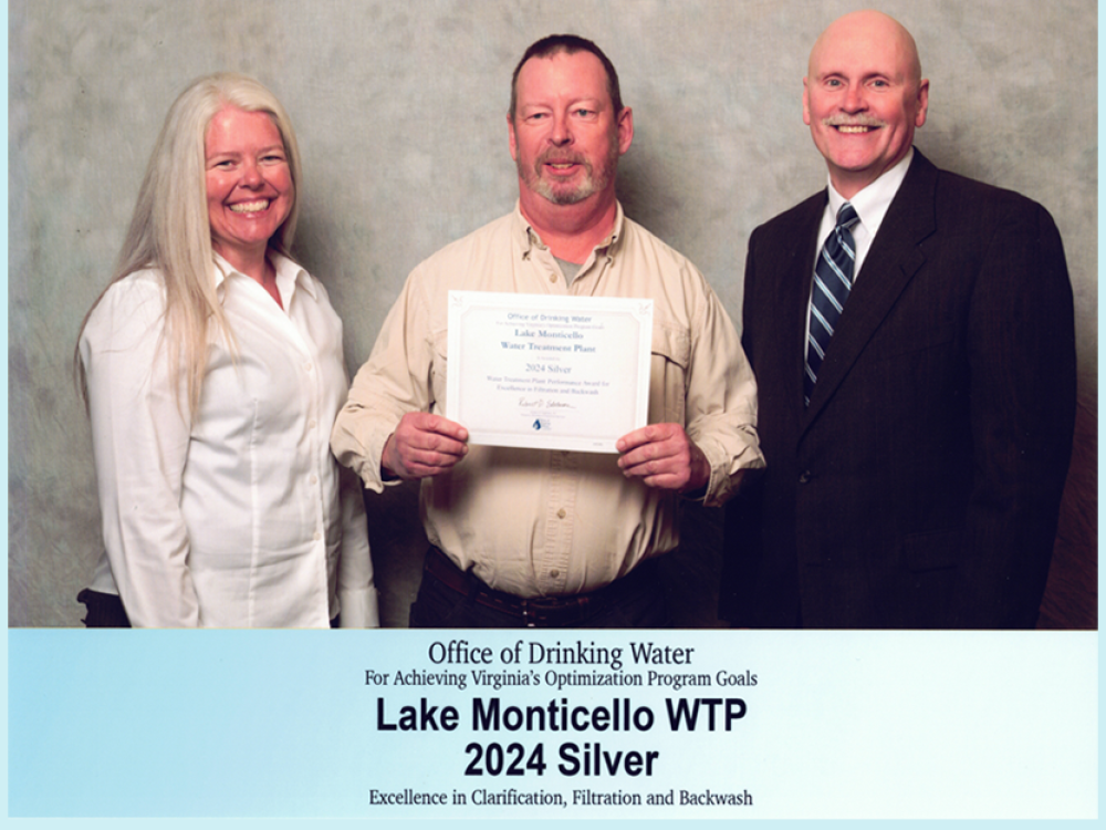 Three individuals standing together with an award in the hands of the middle person.
