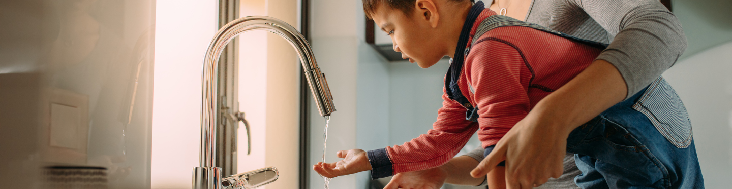 Little boy receiving help from woman washing his hands